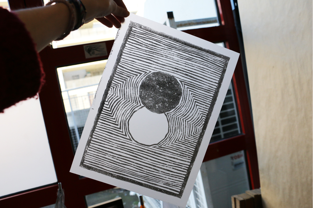 Linogravure à l'encre noire réalisée sur un papier calque. Une jeune fille tient l'illustration face à une fenêtre afin de mettre en valeur la transparence du papier calque.