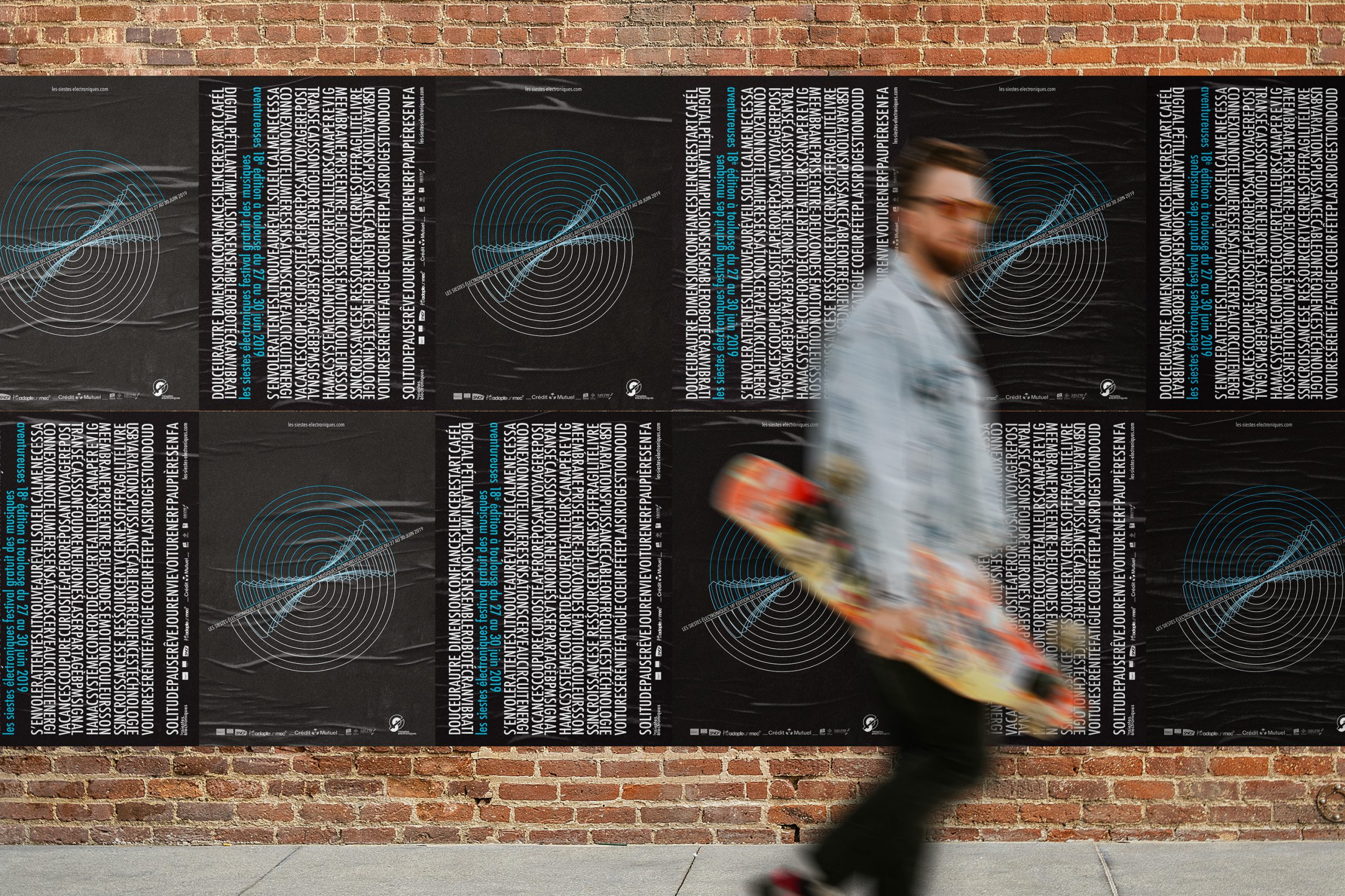 Photographie d'un homme passant devant un long mur sur lequel se trouve 10 affiches des siestes électroniques en versions bleue.