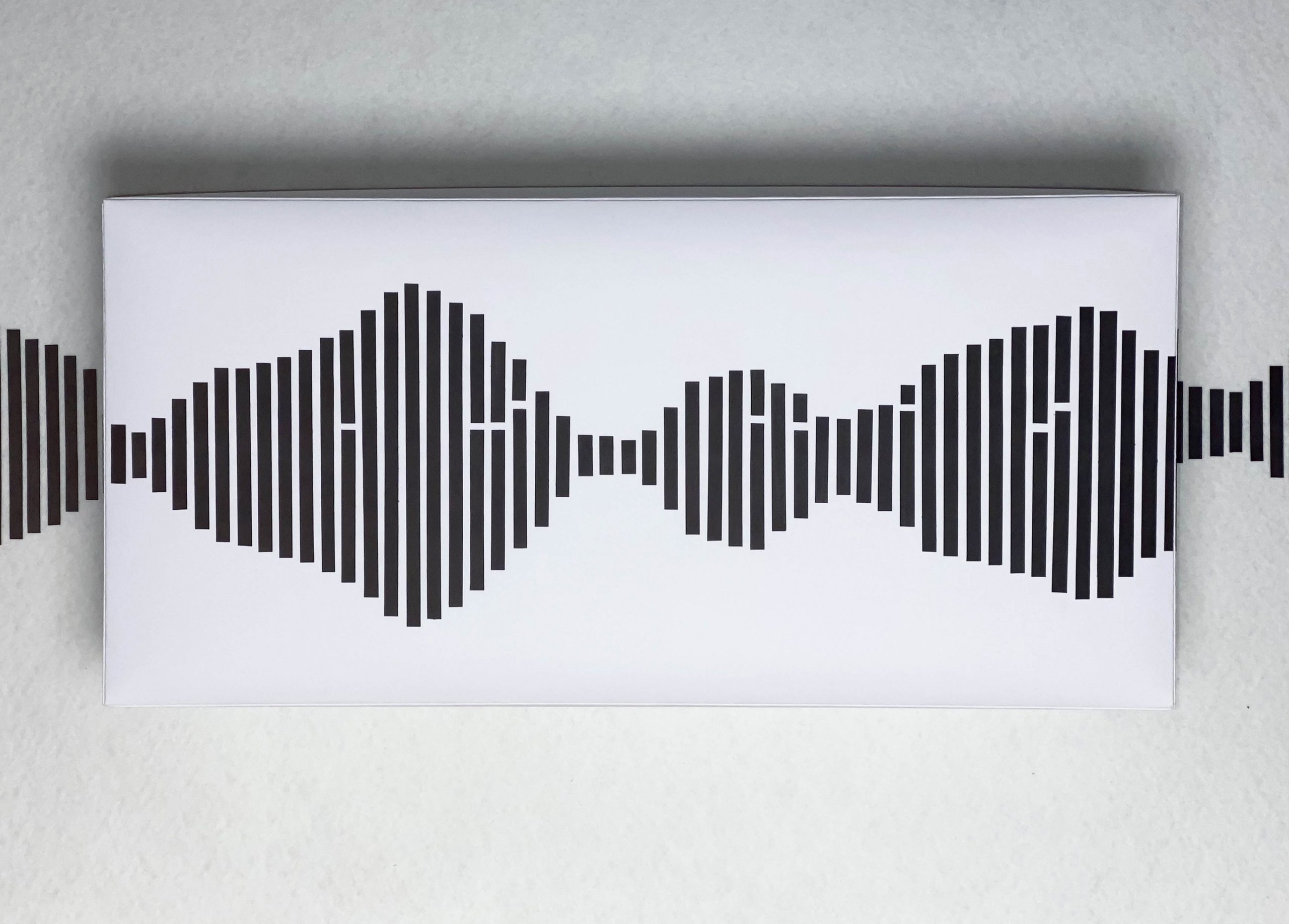 Vue de face du luminaire, éteint. On ne voit donc qu'un rectangle blanc en 3d, sur lequel sont collées des bandes de papier noir formant une vague d'onde sonore.